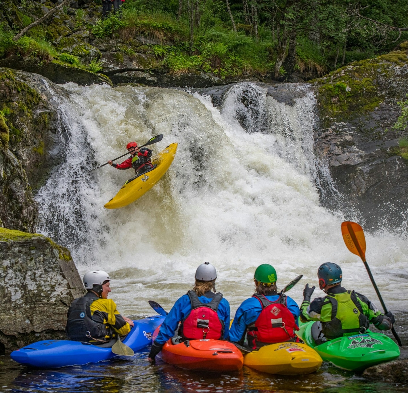 A group of people in kayaks sitting by a waterfall.